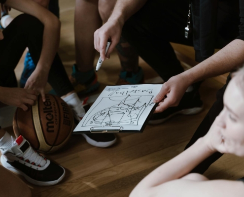 Close-up of a basketball team huddling with the coach discussing strategy indoors.