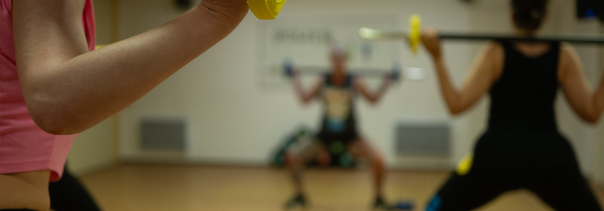 Close-up of a person gripping a barbell with a yellow weight plate during a group workout in a gym