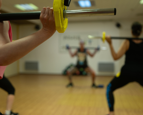 Close-up of a person gripping a barbell with a yellow weight plate during a group workout in a gym