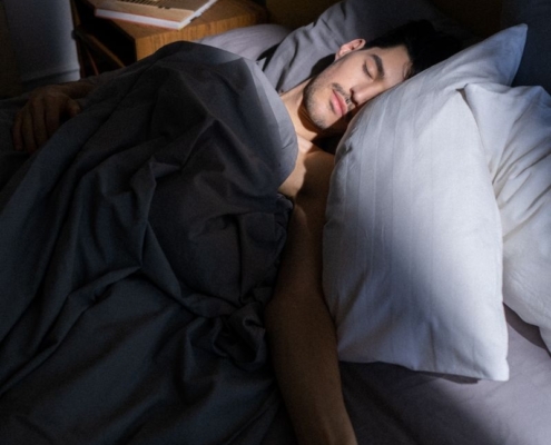 A man sleeps peacefully in a sunlit bedroom, with soft shadows cast on his face.