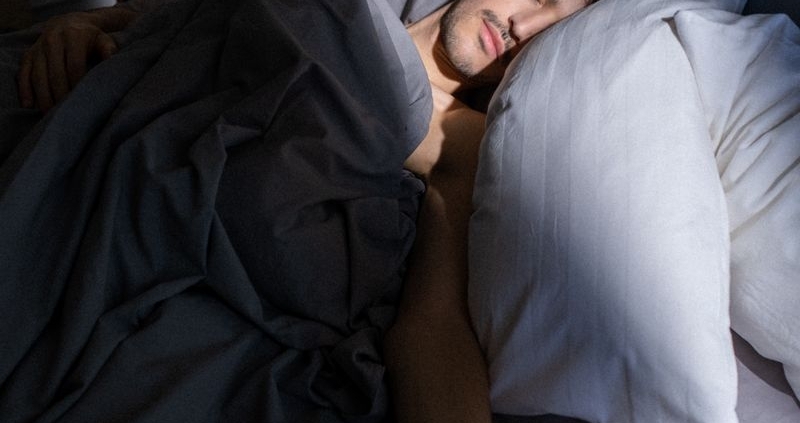A man sleeps peacefully in a sunlit bedroom, with soft shadows cast on his face.