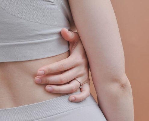 A close-up shot showing a woman's hand on her back in a studio setting, emphasizing texture and form.