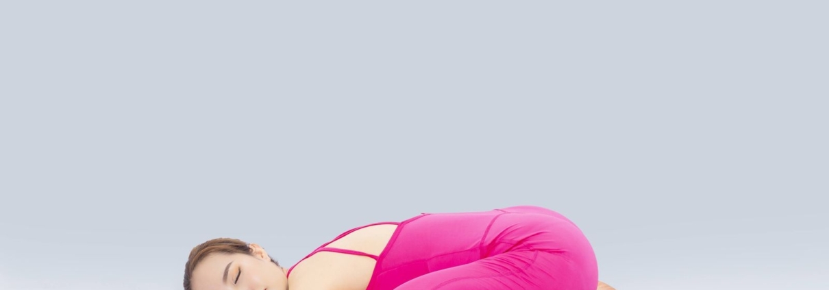 Woman doing yoga indoors in a pink outfit, demonstrating the child's pose for wellness and relaxation.