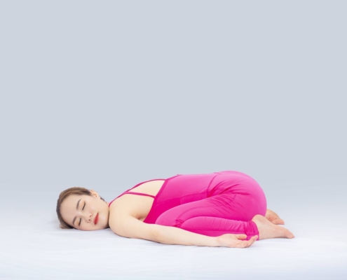 Woman doing yoga indoors in a pink outfit, demonstrating the child's pose for wellness and relaxation.