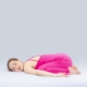 Woman doing yoga indoors in a pink outfit, demonstrating the child's pose for wellness and relaxation.