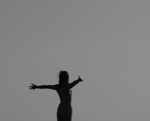 Black and white silhouette of a woman standing with open arms on a fence, symbolizing freedom.
