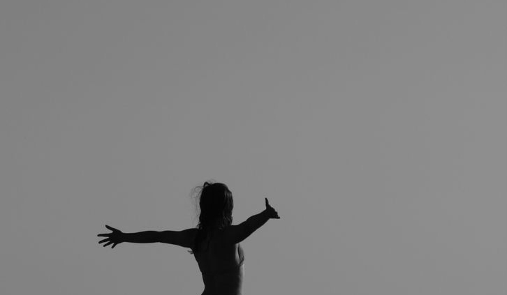Black and white silhouette of a woman standing with open arms on a fence, symbolizing freedom.