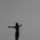 Black and white silhouette of a woman standing with open arms on a fence, symbolizing freedom.
