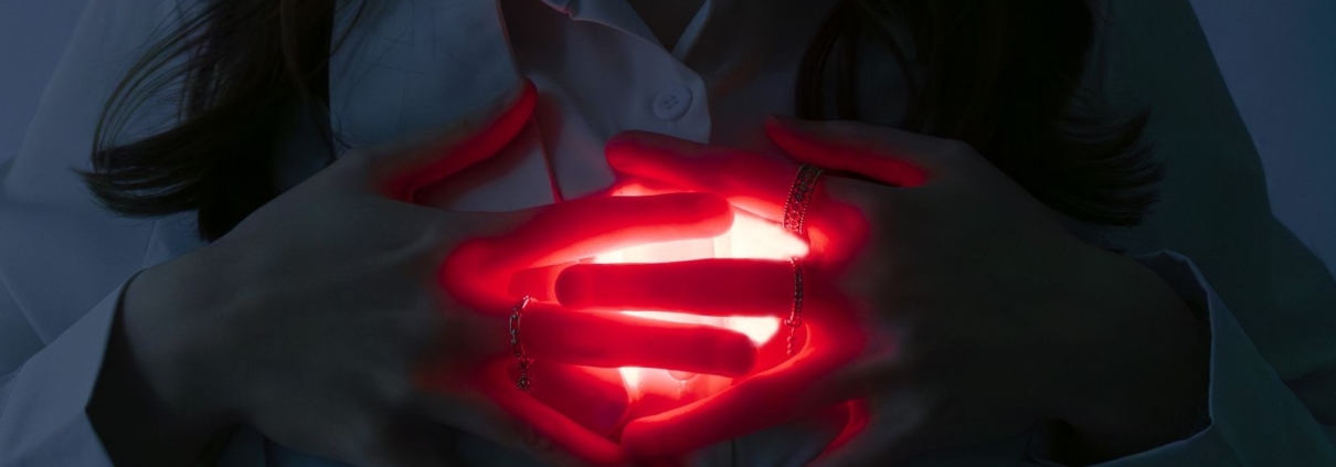 A close-up of hands holding a glowing red heart, symbolizing love and energy.