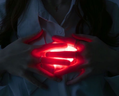 A close-up of hands holding a glowing red heart, symbolizing love and energy.