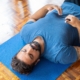 Adult man lying on a blue yoga mat indoors with eyes closed, focusing on relaxation and mindfulness.