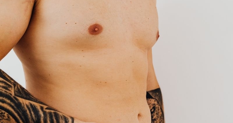 Close-up of a shirtless man measuring his waist with a pink tape measure in a studio setting.