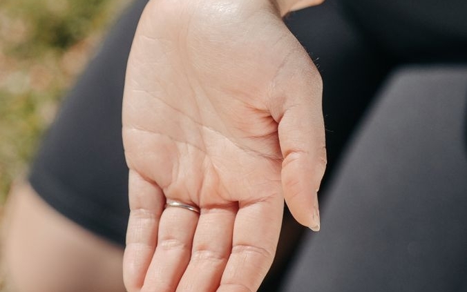 Close-up of a woman's hand holding her wrist outdoors, symbolizing injury or pain relief.