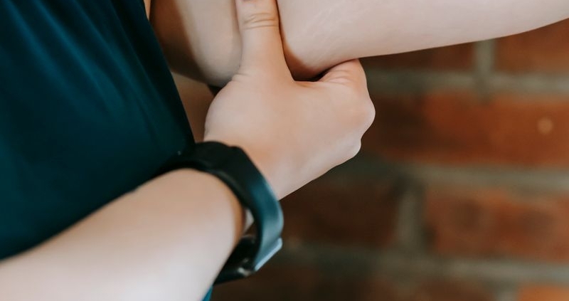 Crop unrecognizable plus size female showing weak arm against brick wall in gym