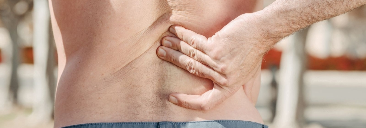 Close-up of a man holding his lower back in pain, possibly indicating discomfort or injury.